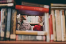 people smiling at each other through a gap in books in a library